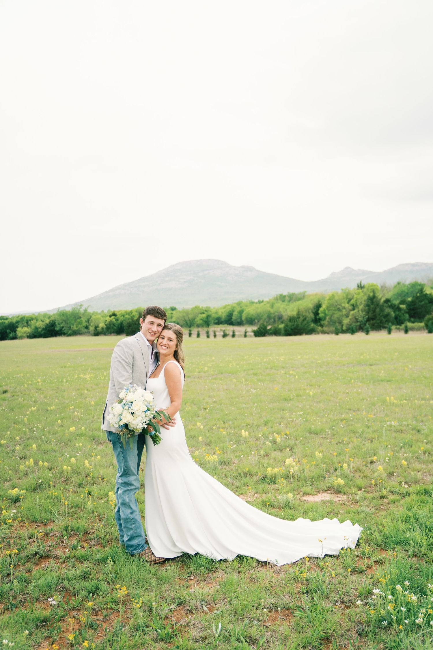 Couple in wedding attire share intimate moment in mountain meadow filled with wildflowers.