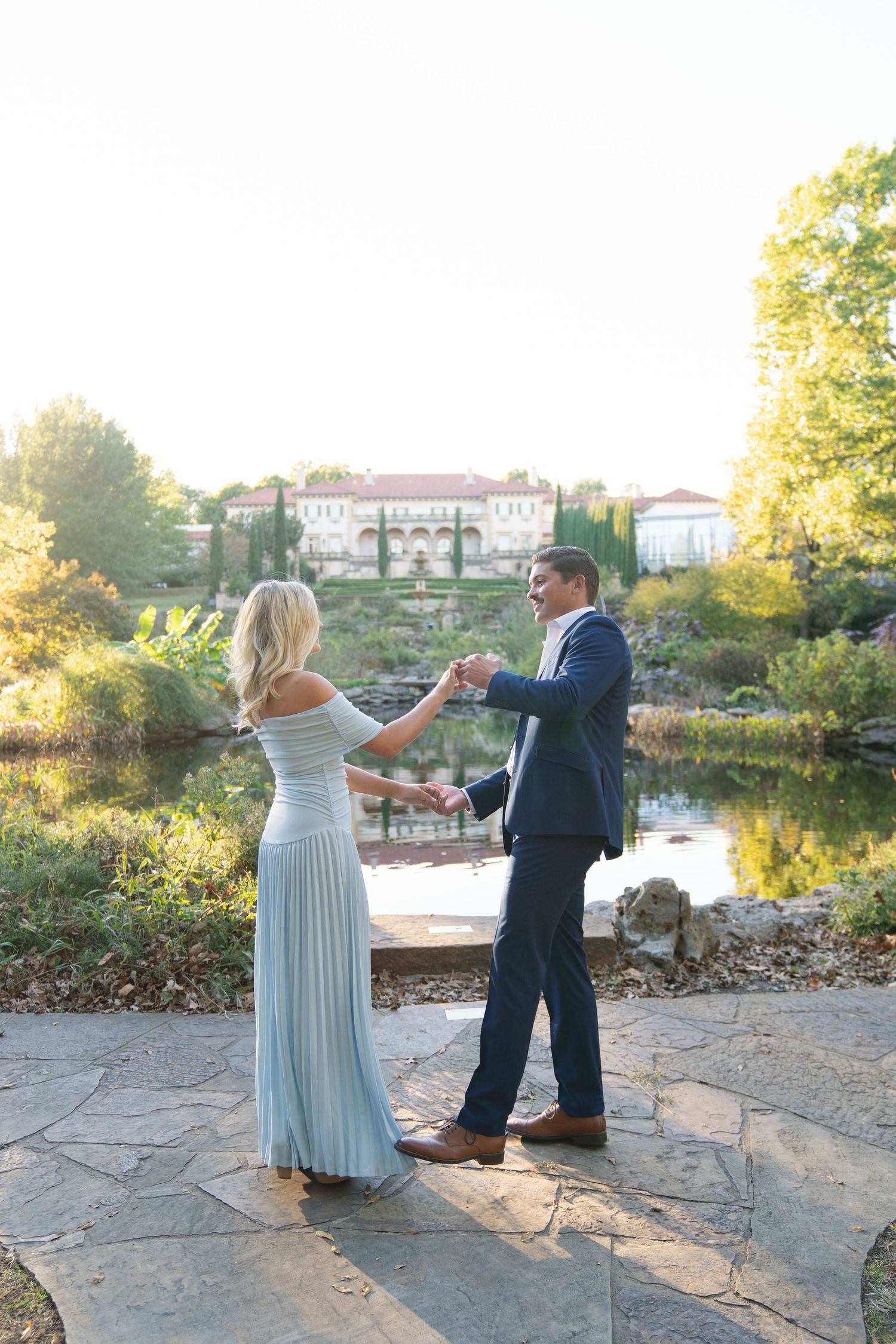 A couple dances together by a scenic waterfront during sunset.