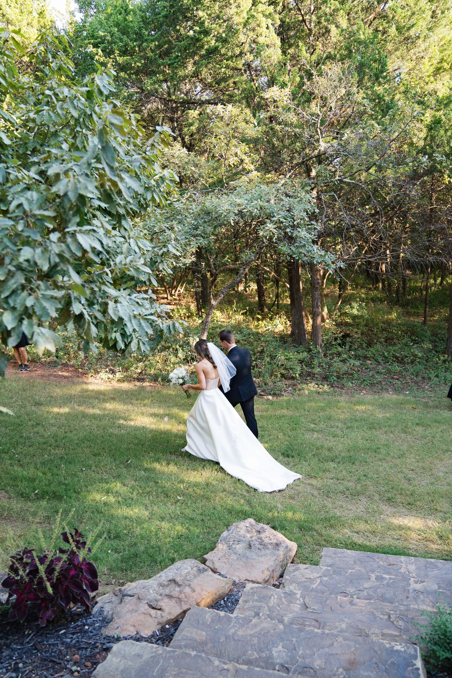 Wedding couple posing for photos on stone steps in a scenic outdoor garden setting.