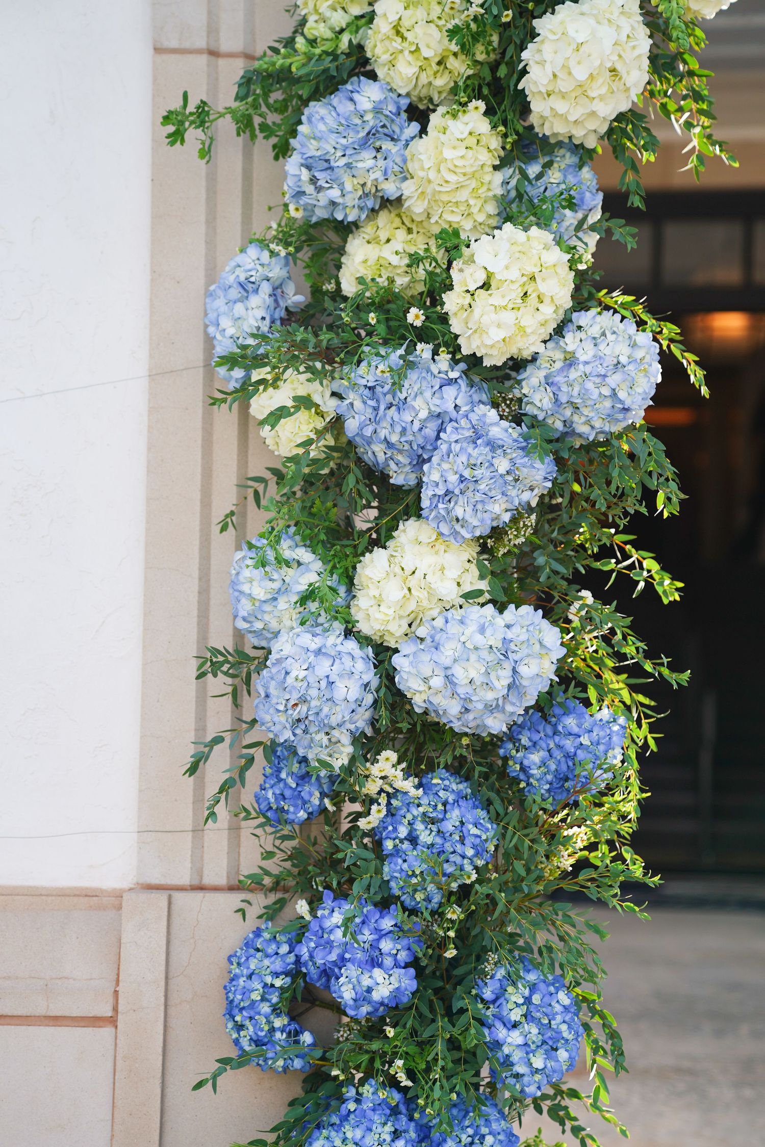 Beautiful floral arch arrangement with blue and white hydrangeas and greenery.