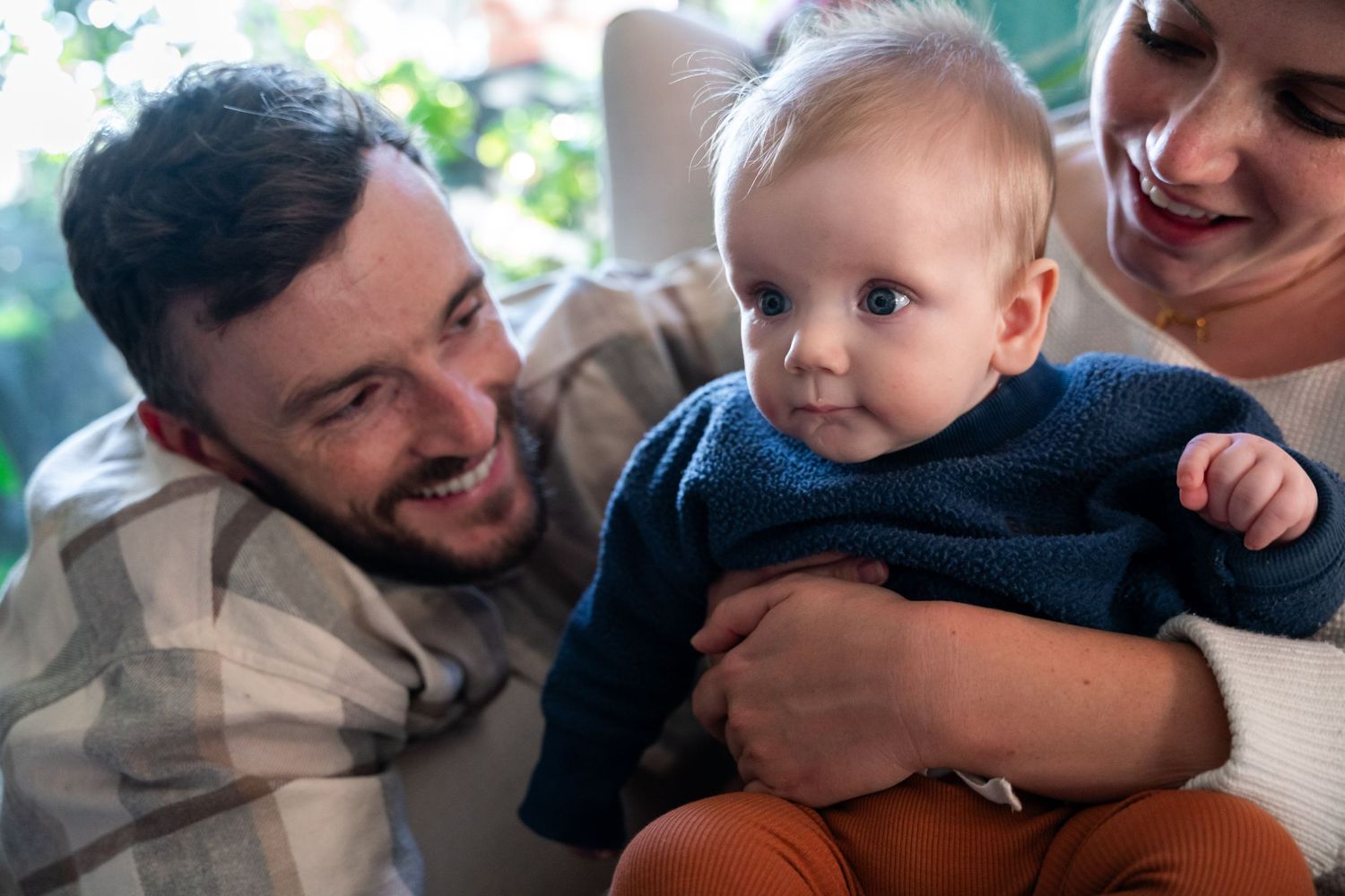 A baby in a navy sweater shares a joyful moment with adults during a casual family gathering.