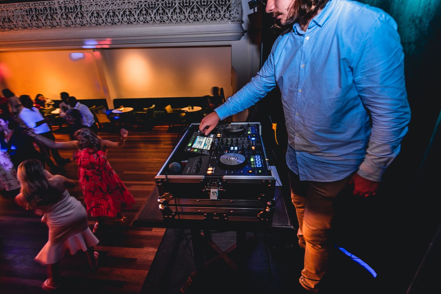 DJ performing at a nightclub with colorful lighting and people dancing in the background.