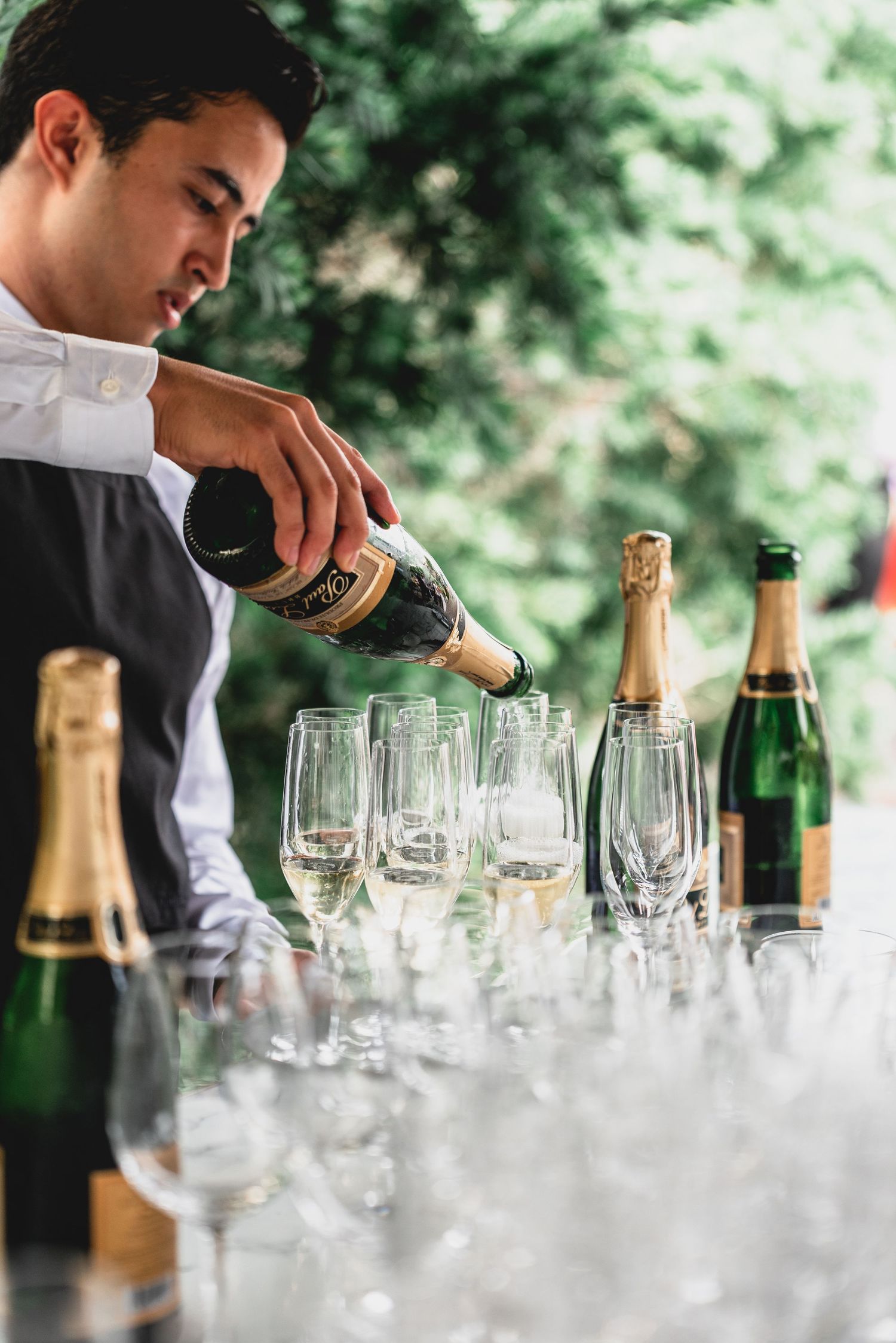 A bartender pours champagne into elegant crystal glasses at an upscale event with multiple bottles on display.