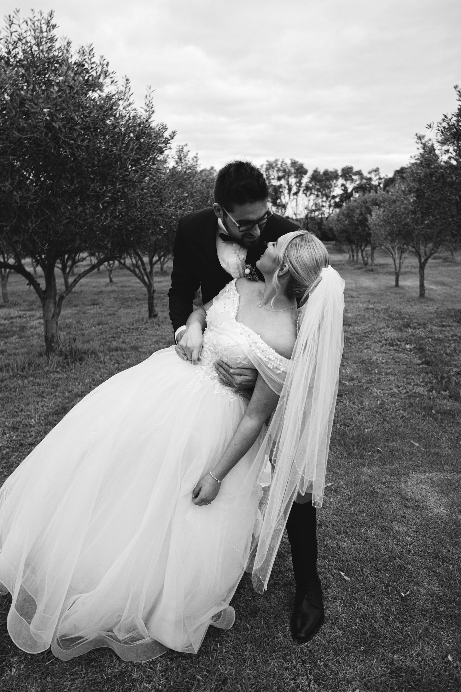 A romantic black and white photo sequence of a couple dancing and dipping in an orchard setting.