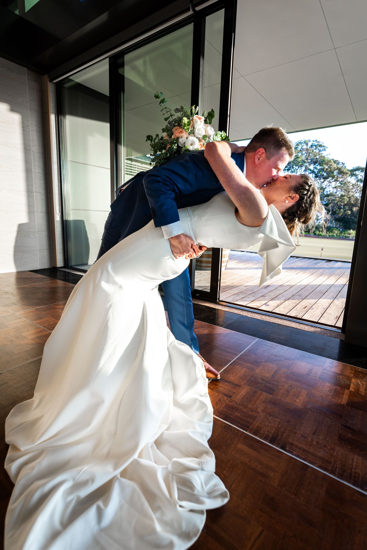 Romantic wedding dance dip sequence captured in modern venue with glass windows.