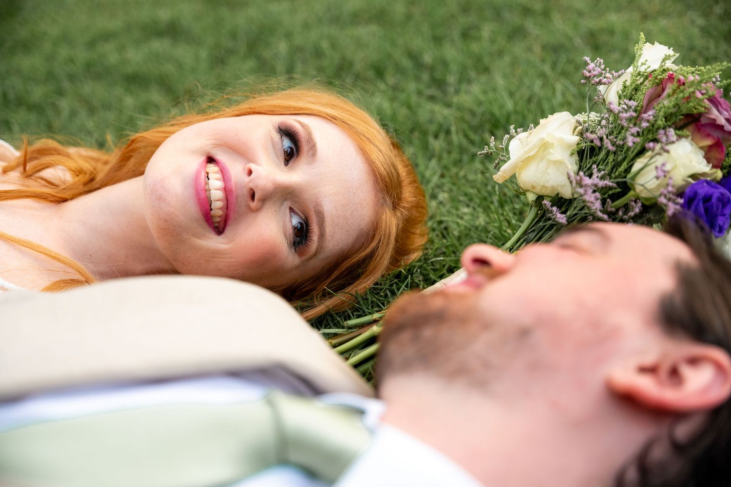 Newlyweds lying on lush green grass during outdoor wedding photo session.