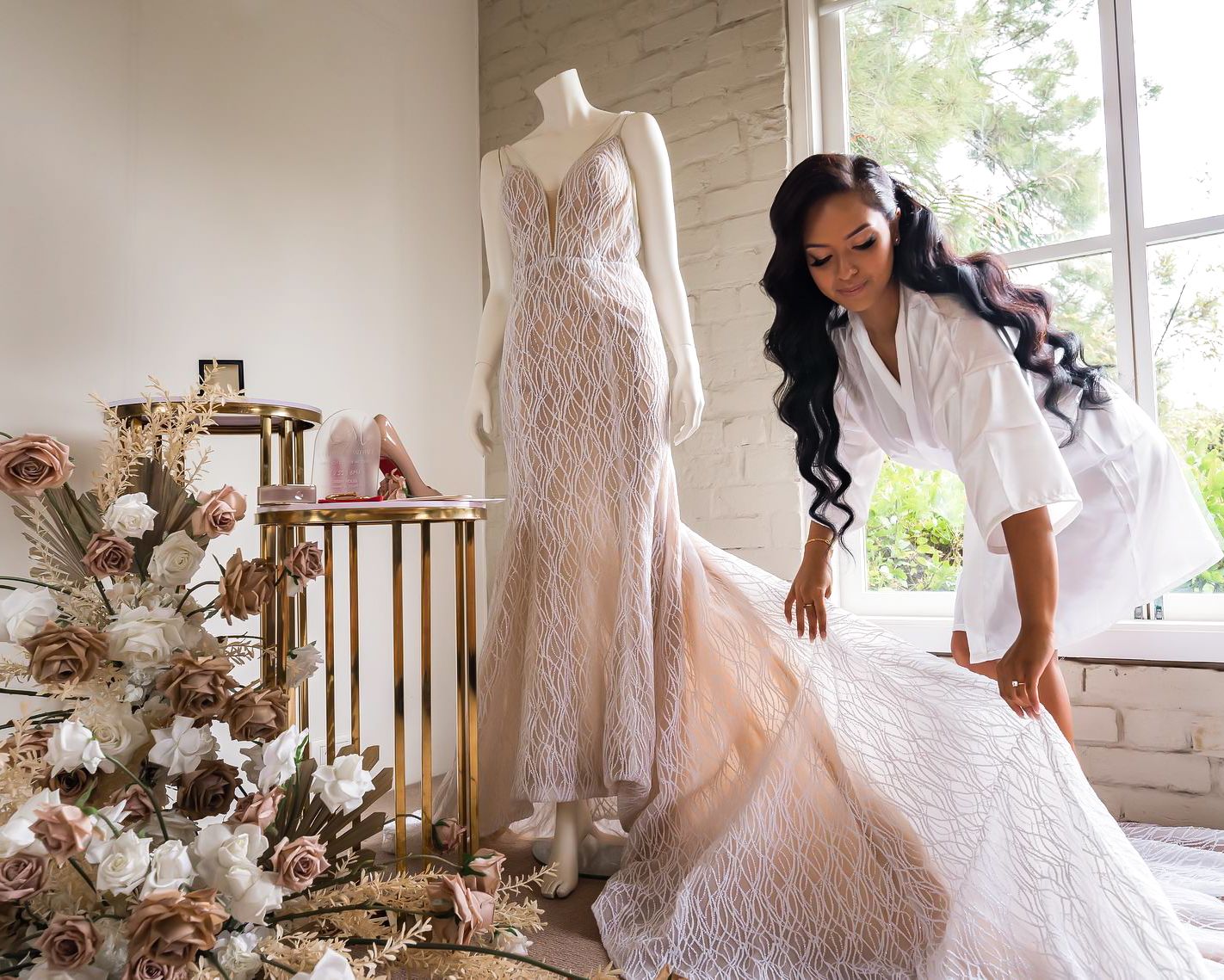 Elegant bridal boutique interior with lace wedding dress on mannequin and floral arrangements by staircase.