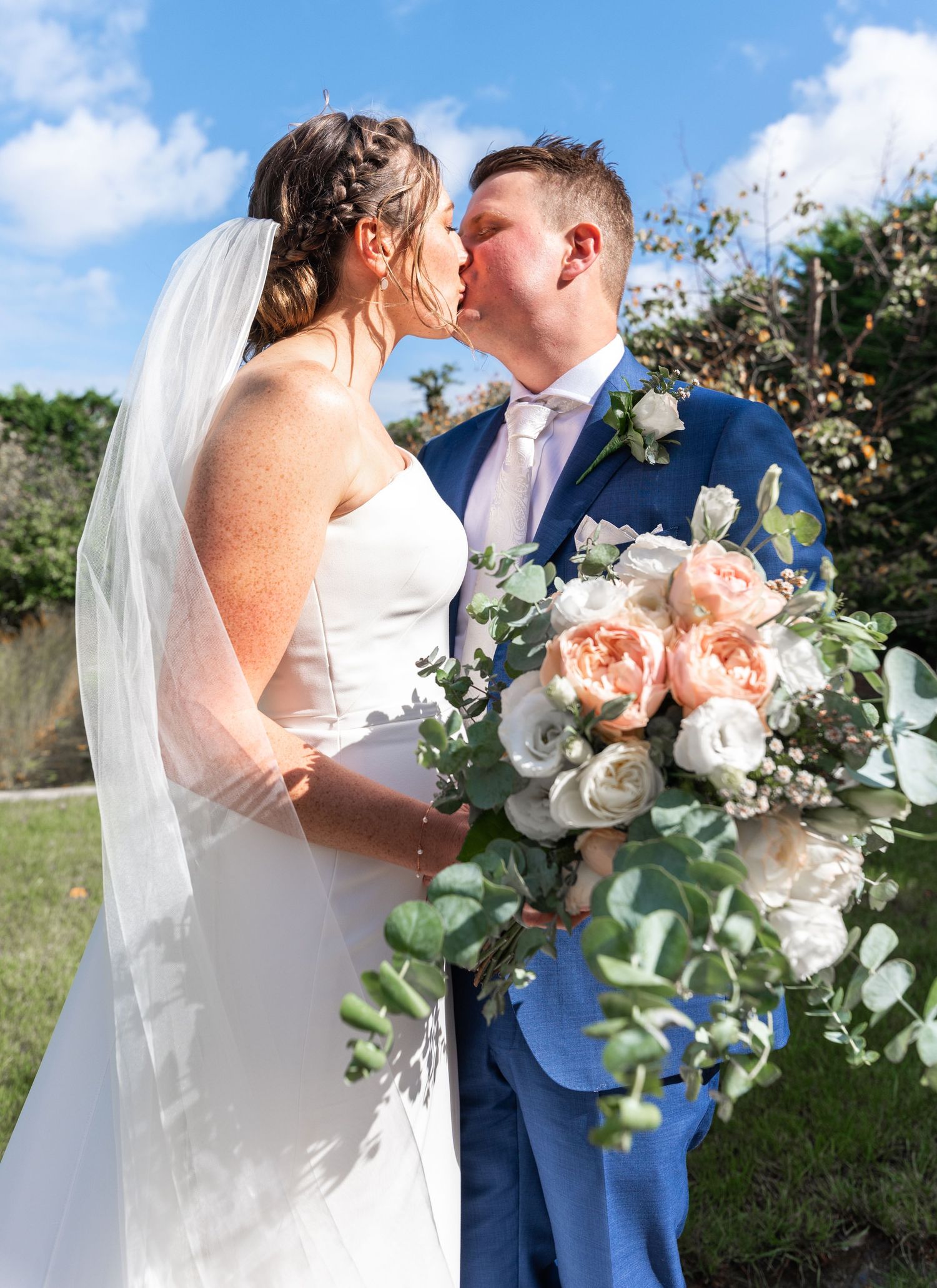 A bride and groom share intimate moments in a garden setting with soft pink and white floral bouquets.