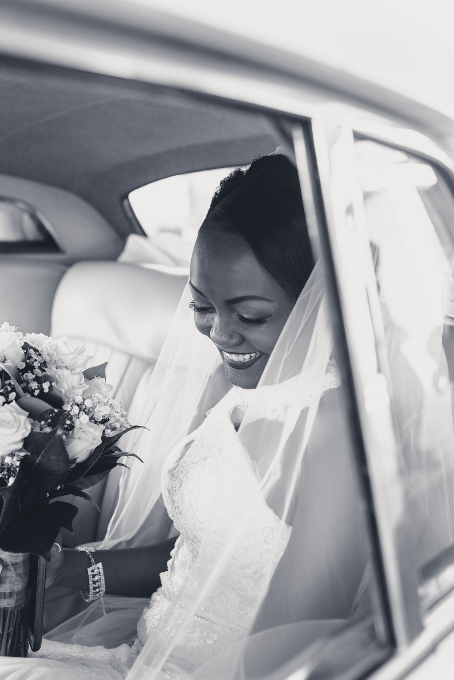 A bride wearing a white veil sits in a car on her wedding day, radiating joy and anticipation.