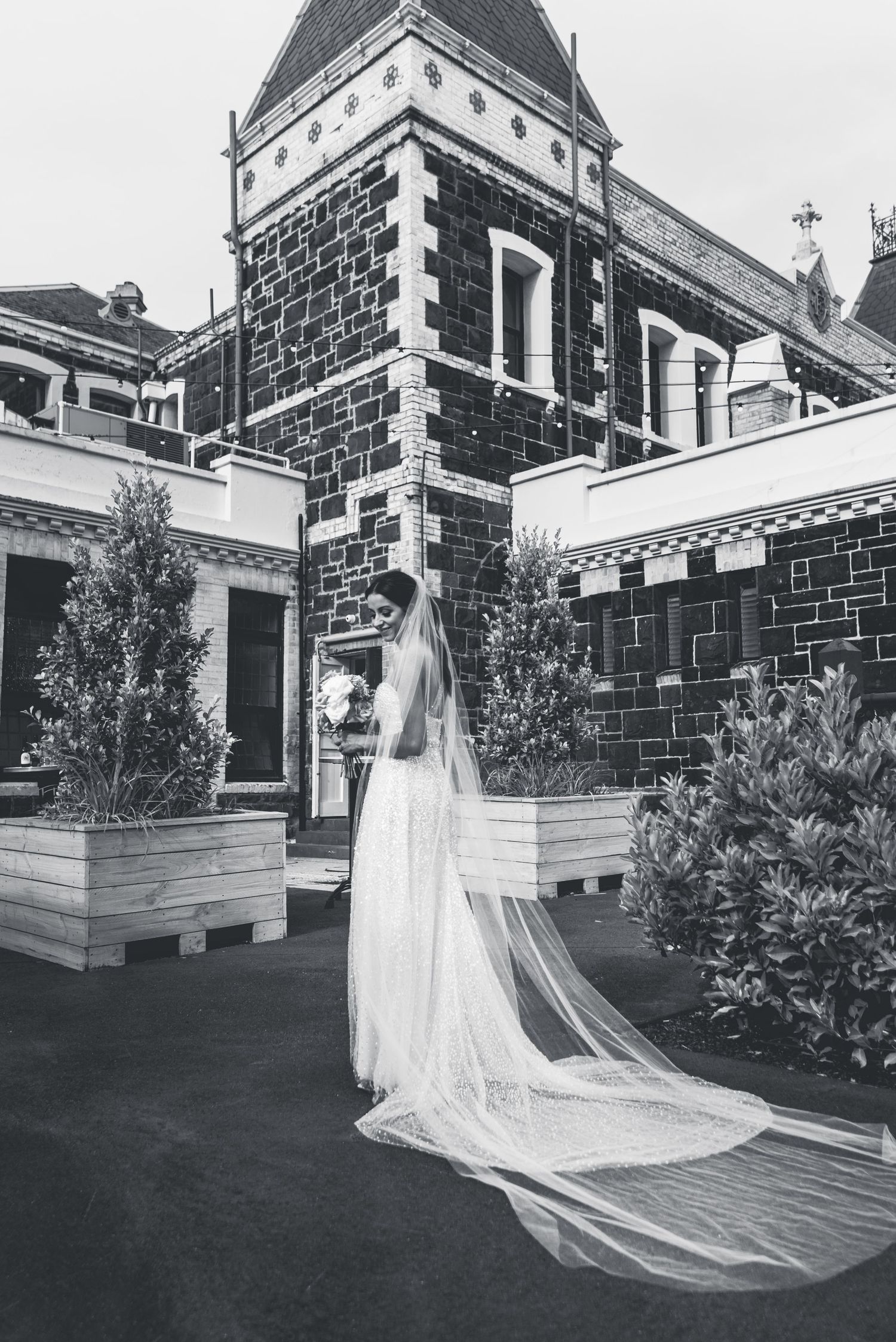 A flowing white wedding dress and veil photographed from multiple angles outside a historic brick building.
