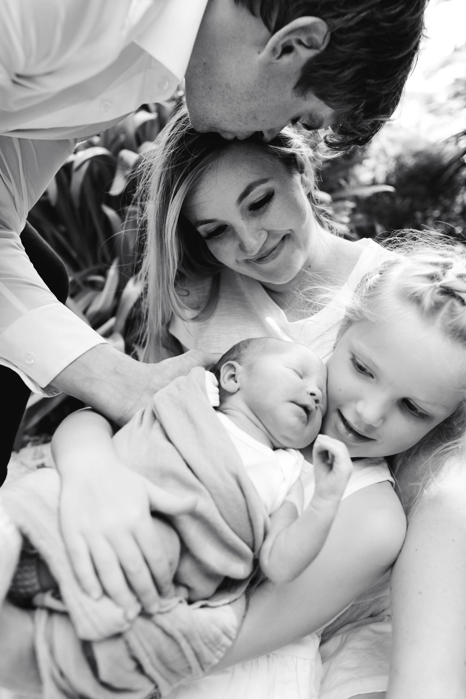 Intimate black and white family portrait showing tender moments with sleeping baby.