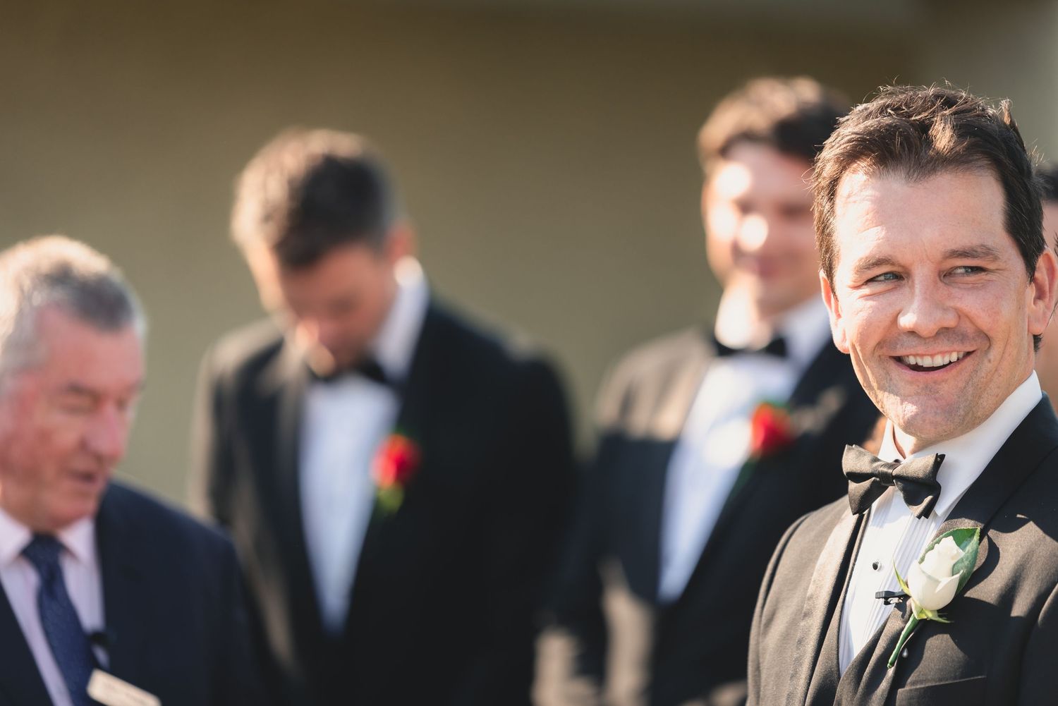 A line of groomsmen in dark suits with white boutonnieres stand together at a formal wedding ceremony.
