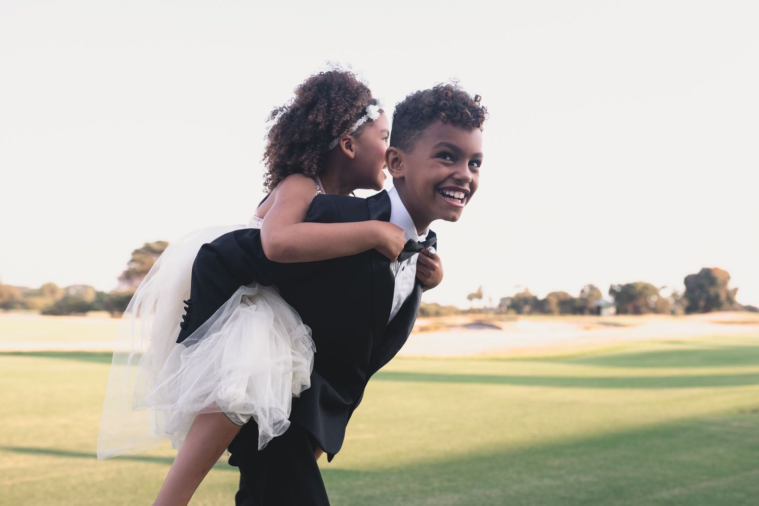 Two people share a joyful piggyback moment on a grassy field during golden hour.