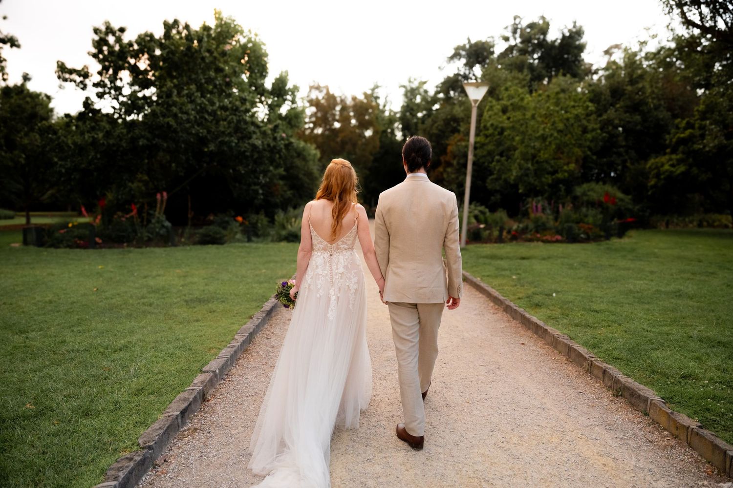 Couple walking along a tree-lined path at sunset after their wedding ceremony.