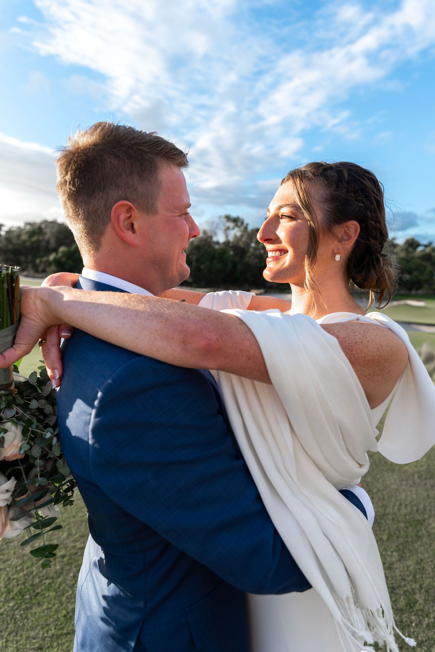 A couple in wedding attire dances and spins together outdoors under a bright blue sky.
