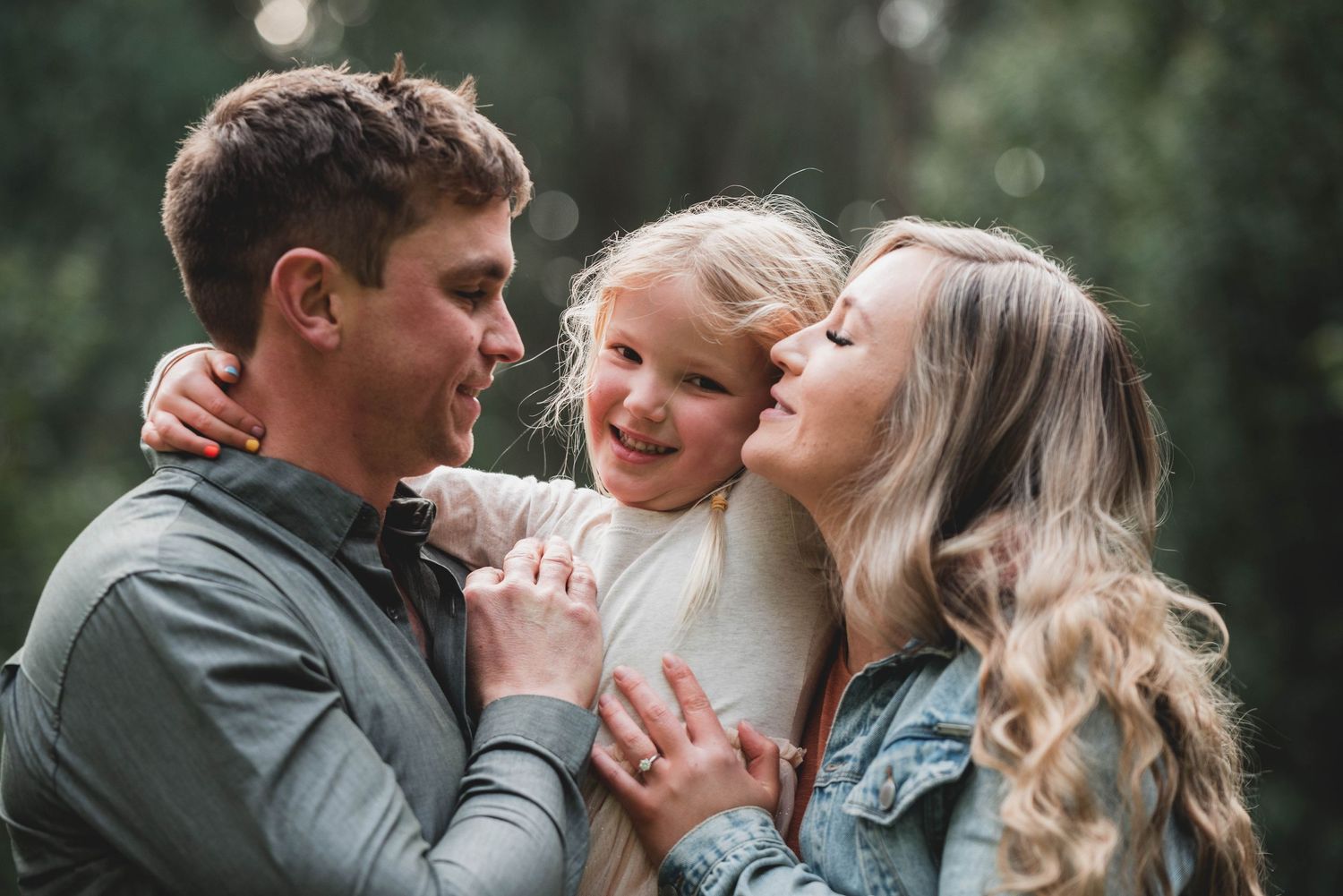 Intimate outdoor photo series showing tender family moments in a natural setting with soft lighting and greenery.