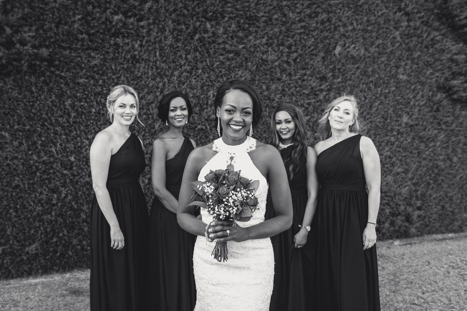 A joyful wedding party in black and white, with bridesmaids in elegant dark dresses surrounding a bride in white holding flowers.