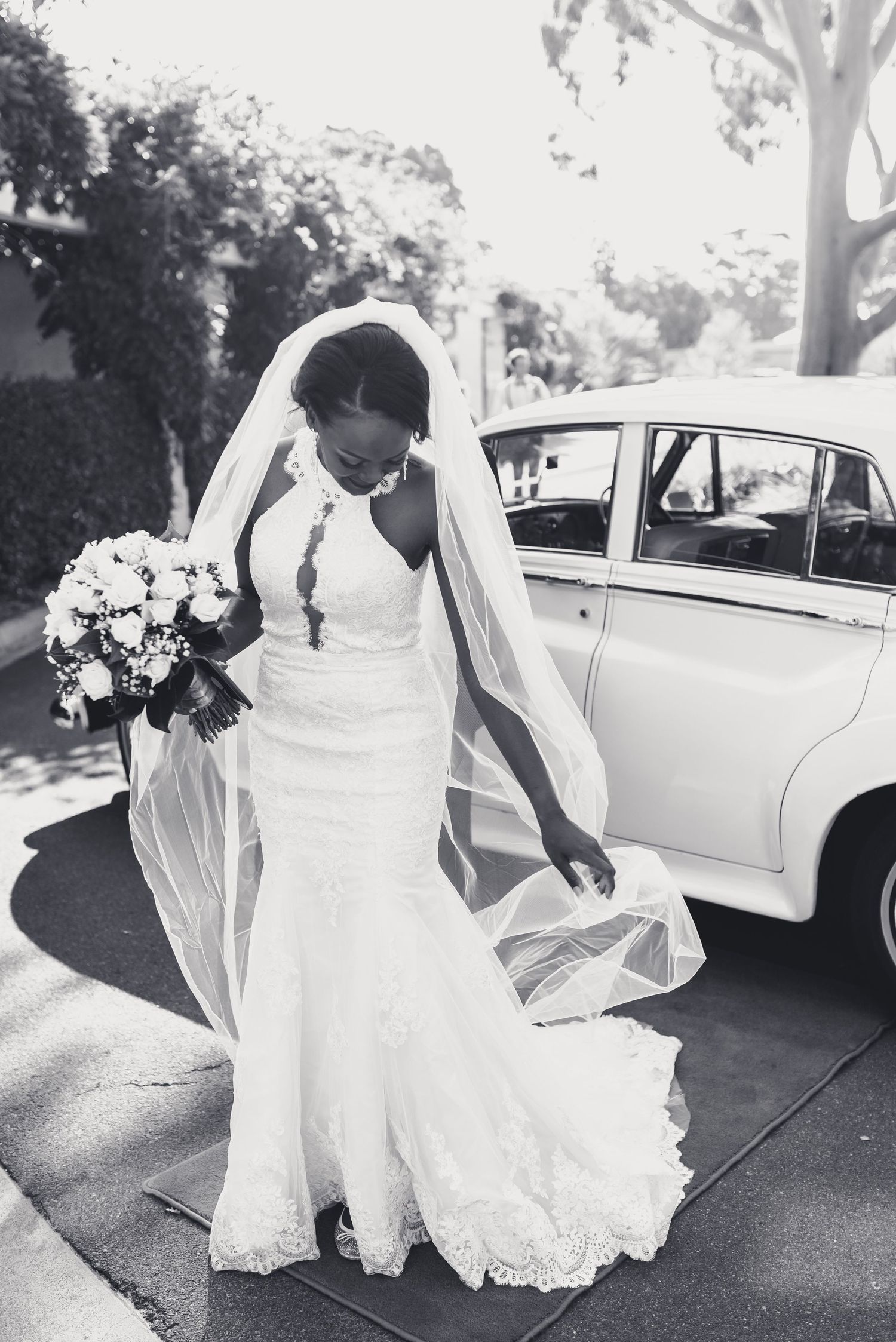 A series of black and white photos showing a bride's flowing white dress and classic car in an outdoor wedding setting.