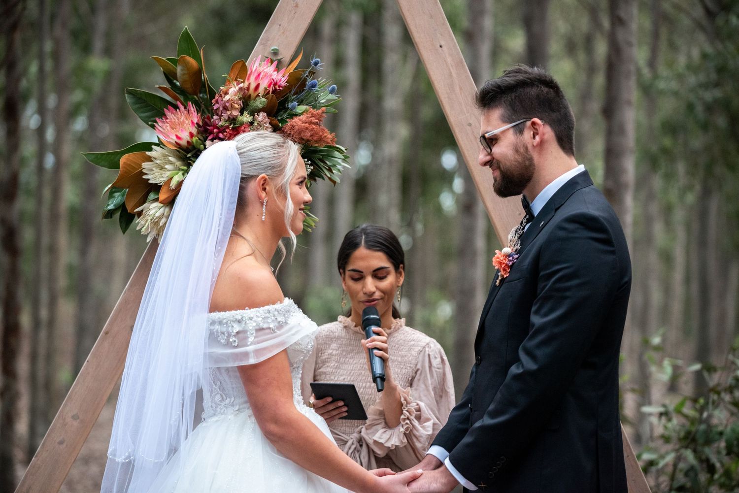 Outdoor wedding ceremony under wooden arch with floral decorations.