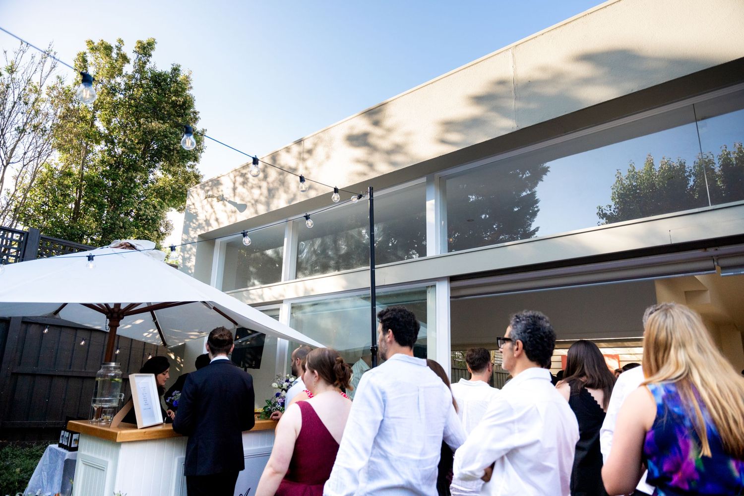 Wedding guests gather outdoors under a white canopy during a daytime celebration.
