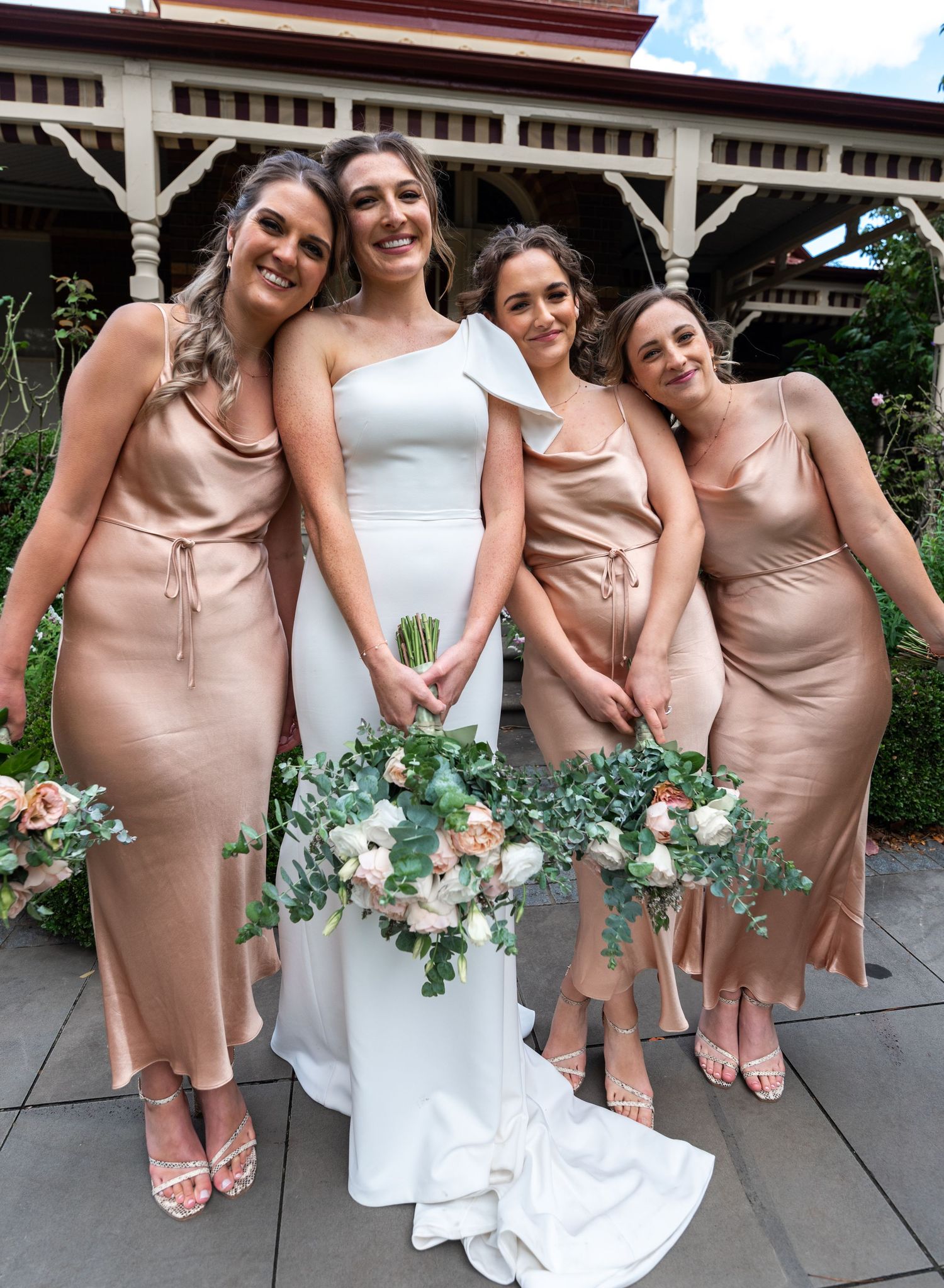 Bridesmaids in blush pink dresses pose together with bouquets on stone patio.