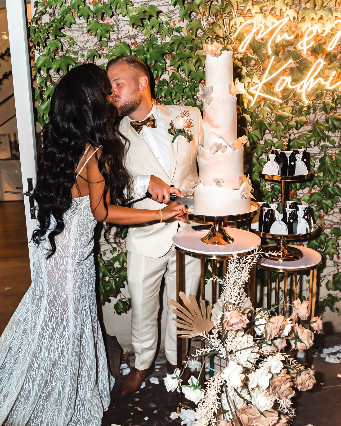 Wedding celebration scene with elegant decor featuring floral arrangements, white cake displays and romantic lighting.