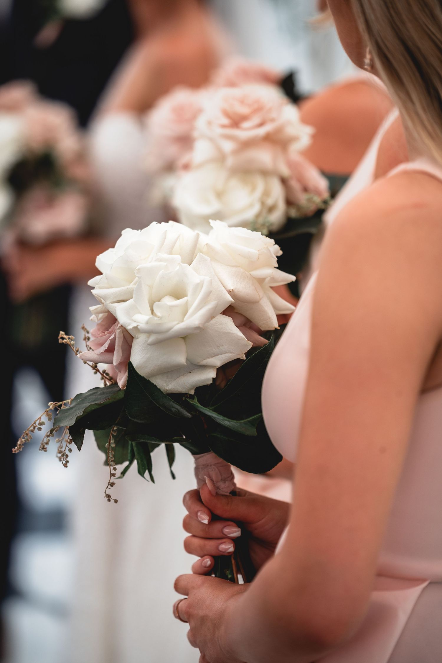 A bridesmaid holds an elegant white and pink rose bouquet at a wedding ceremony.