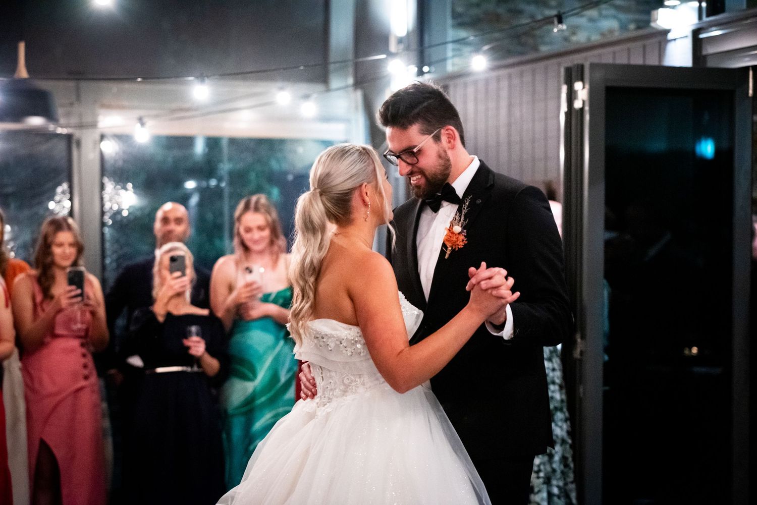 Wedding reception dance floor filled with guests celebrating under dim lighting.