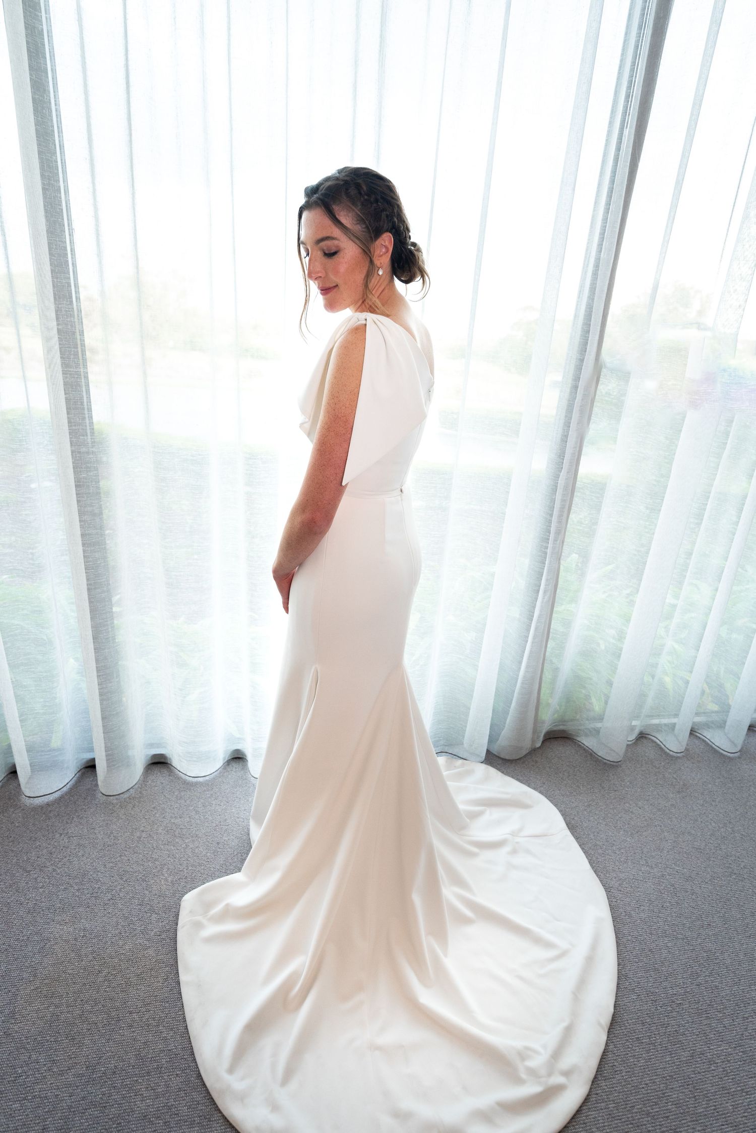 A bride in an elegant white wedding dress with a flowing train poses in front of sheer curtains in multiple angles.