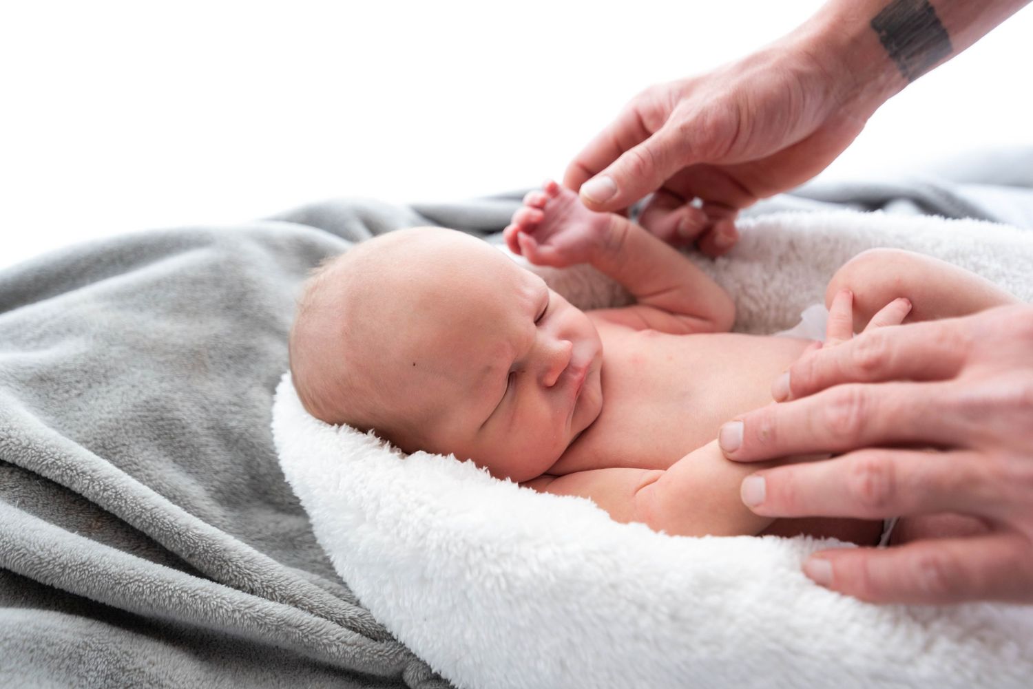 Hands gently massage a sleeping baby lying on a soft gray blanket during an infant massage session.