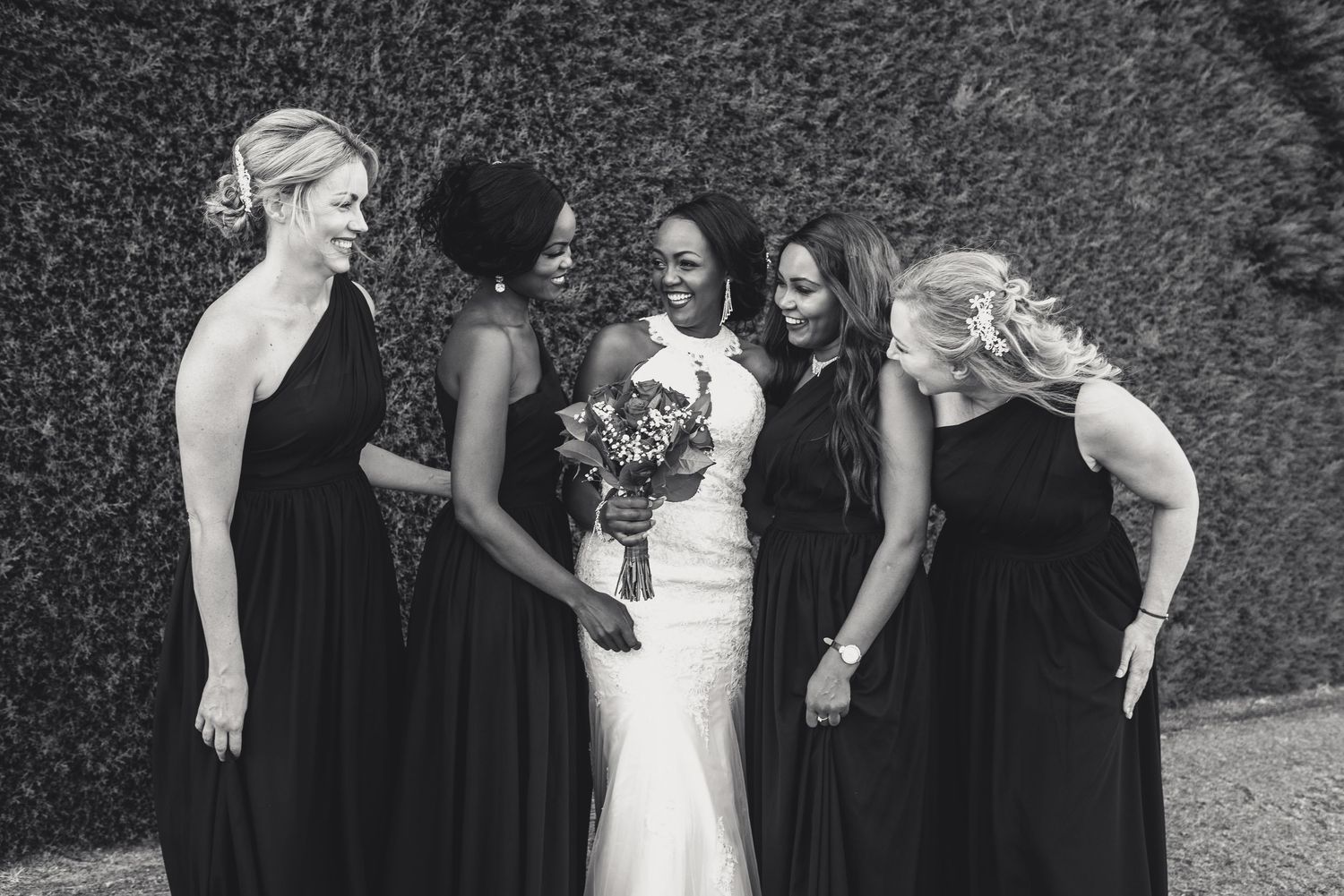 A bridal party in black and white shares a candid laughing moment together outdoors.