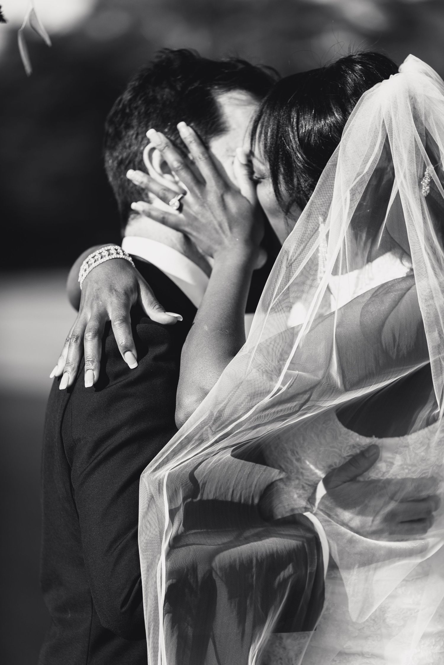 A romantic black and white wedding photo captures a tender kiss between newlyweds, with the bride's veil flowing softly.