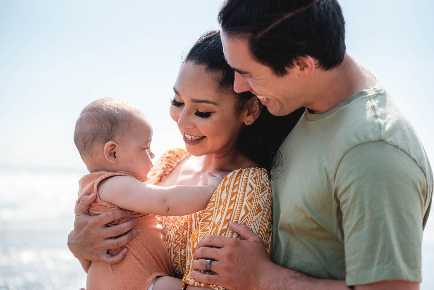 A tender family moment captured in soft natural light showing parents embracing their baby outdoors.