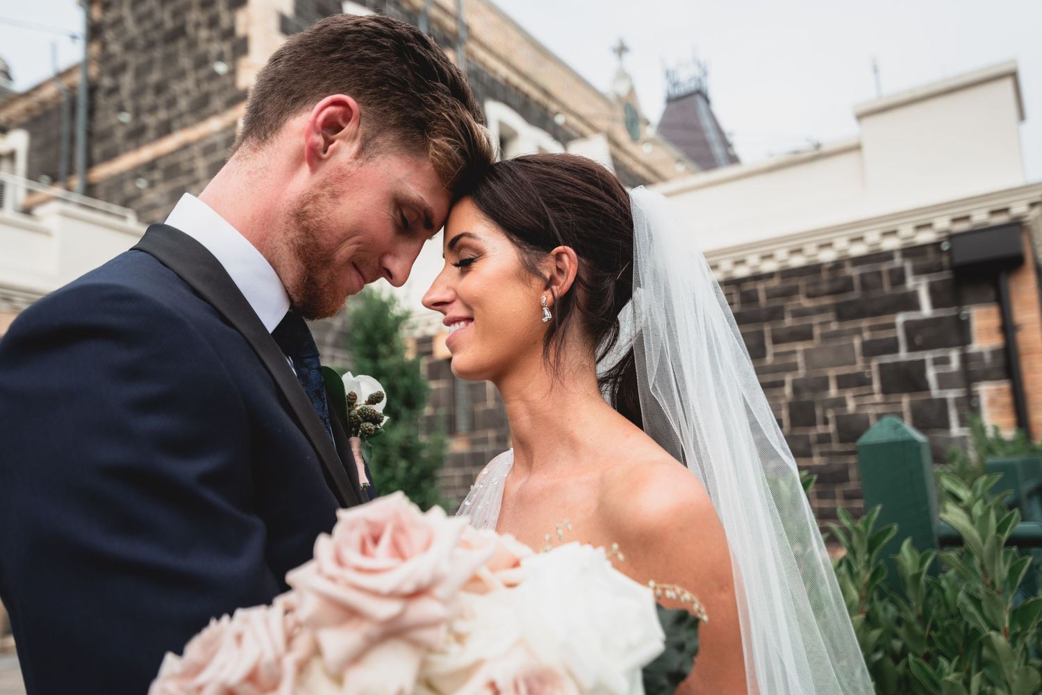 A tender moment between newlyweds sharing an intimate embrace with pink roses and a flowing veil at their wedding.