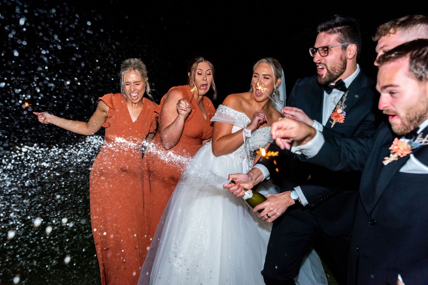Wedding party celebrating with sparklers and confetti at nighttime reception.
