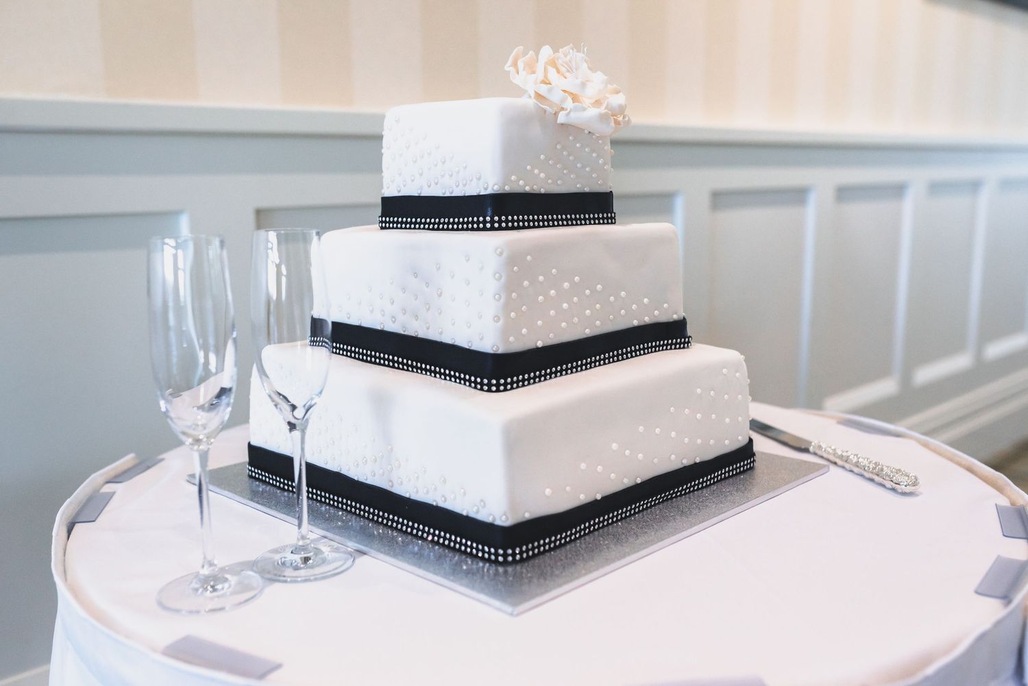 A modern white and black square wedding cake with crystal decorations displayed at an elegant reception venue.