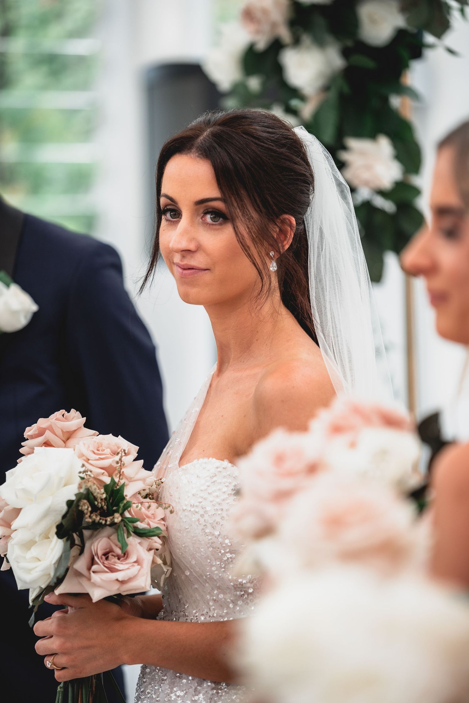 A bride in a white lace wedding dress holds a bouquet of pink and white roses during her wedding ceremony.