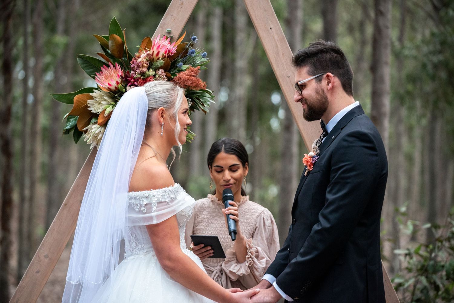 Outdoor forest wedding ceremony with wooden arch decorated with tropical flowers.
