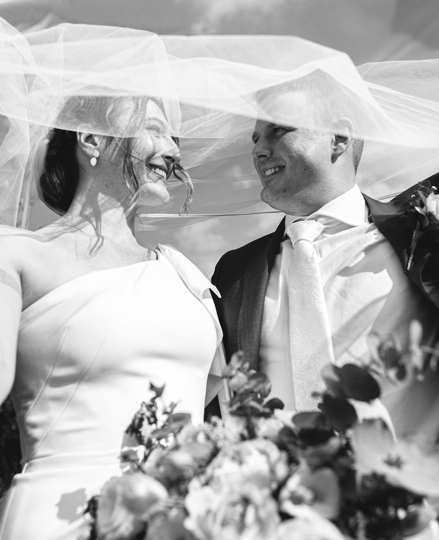 A joyful wedding moment captured in black and white as a couple shares a laugh under a flowing veil.