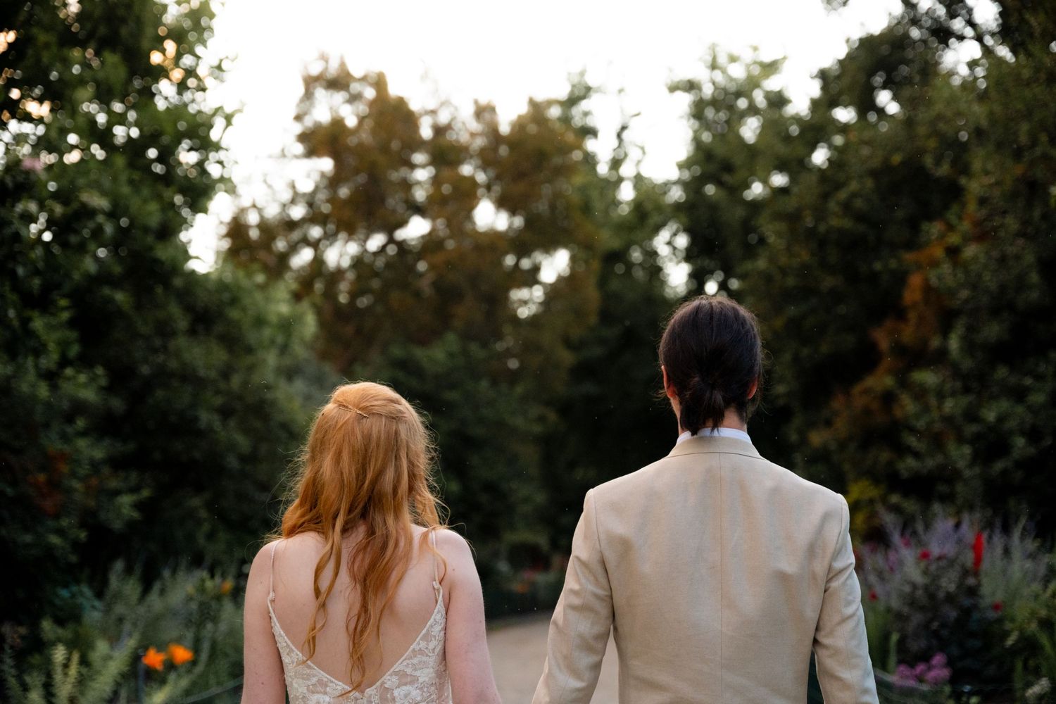 Silhouetted couple walking hand in hand through a garden at sunset after their wedding ceremony.