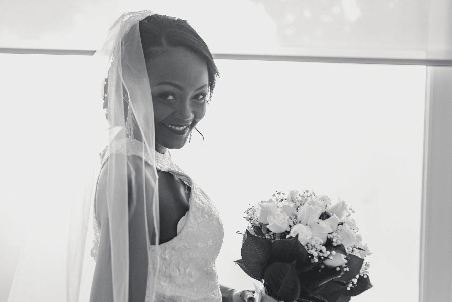 A bride in a white wedding dress and veil holds a bouquet while looking in a mirror.