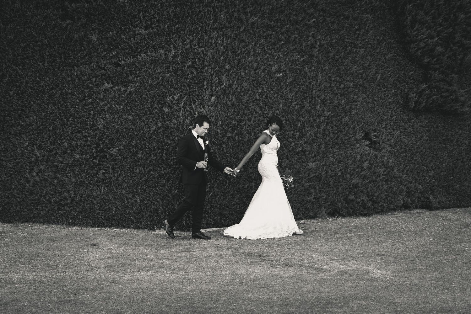 Black and white photo sequence of a couple in wedding attire walking together through a garden setting.