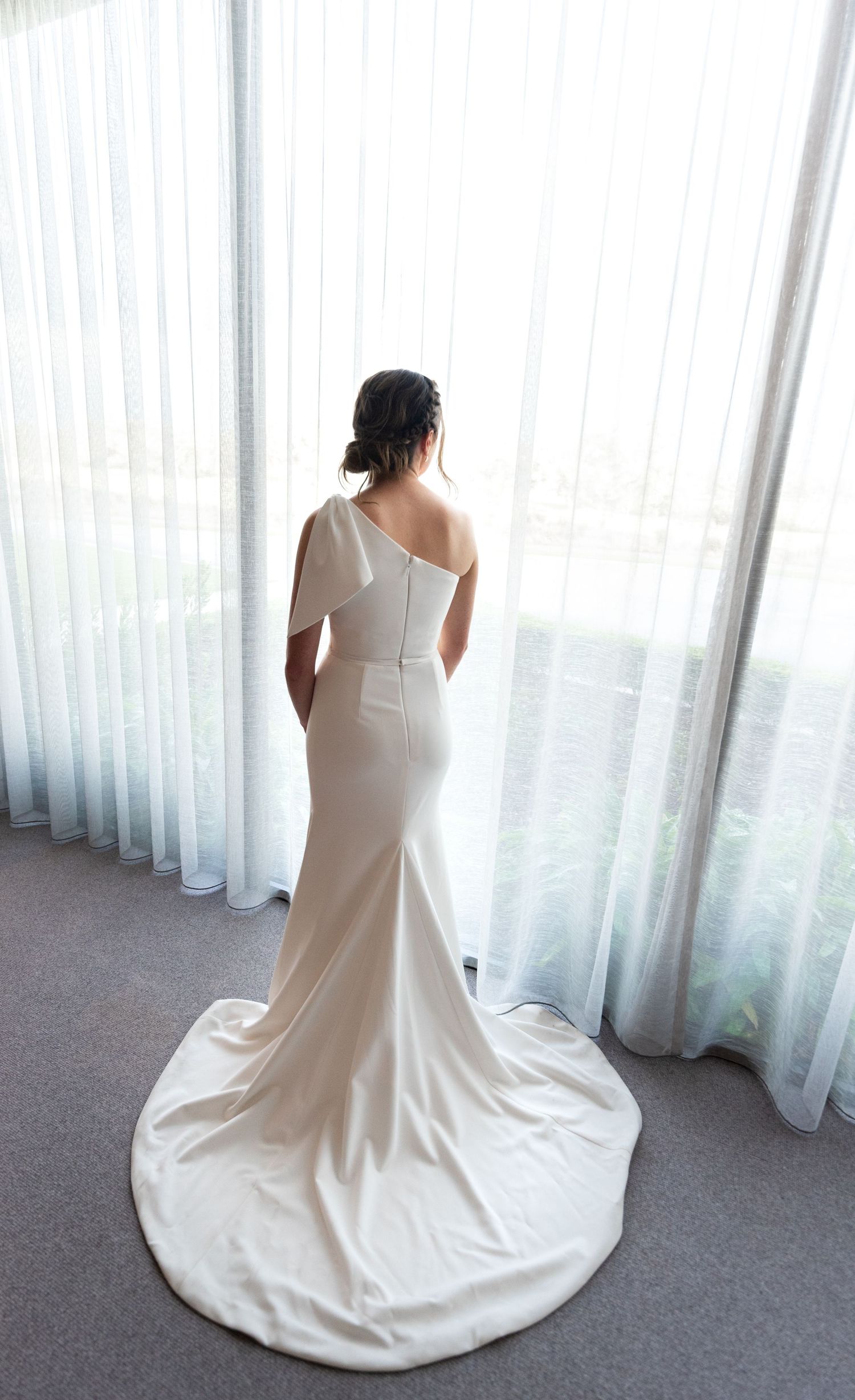 A series of four photos showing the back view of an elegant white wedding dress with a long train against sheer curtains.