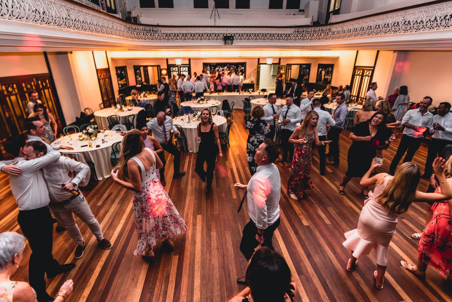 Couples dancing together in a large ballroom during a social dance event with wooden floors and warm lighting.