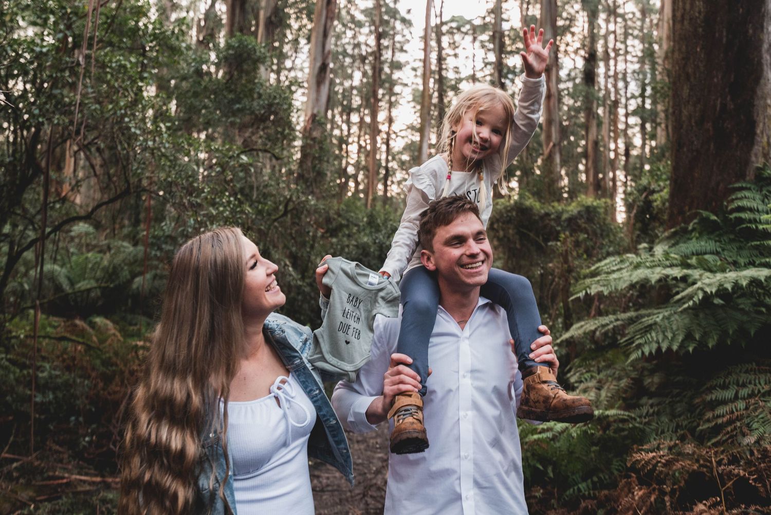A couple shares joyful moments while walking through a lush forest setting during a photo session.
