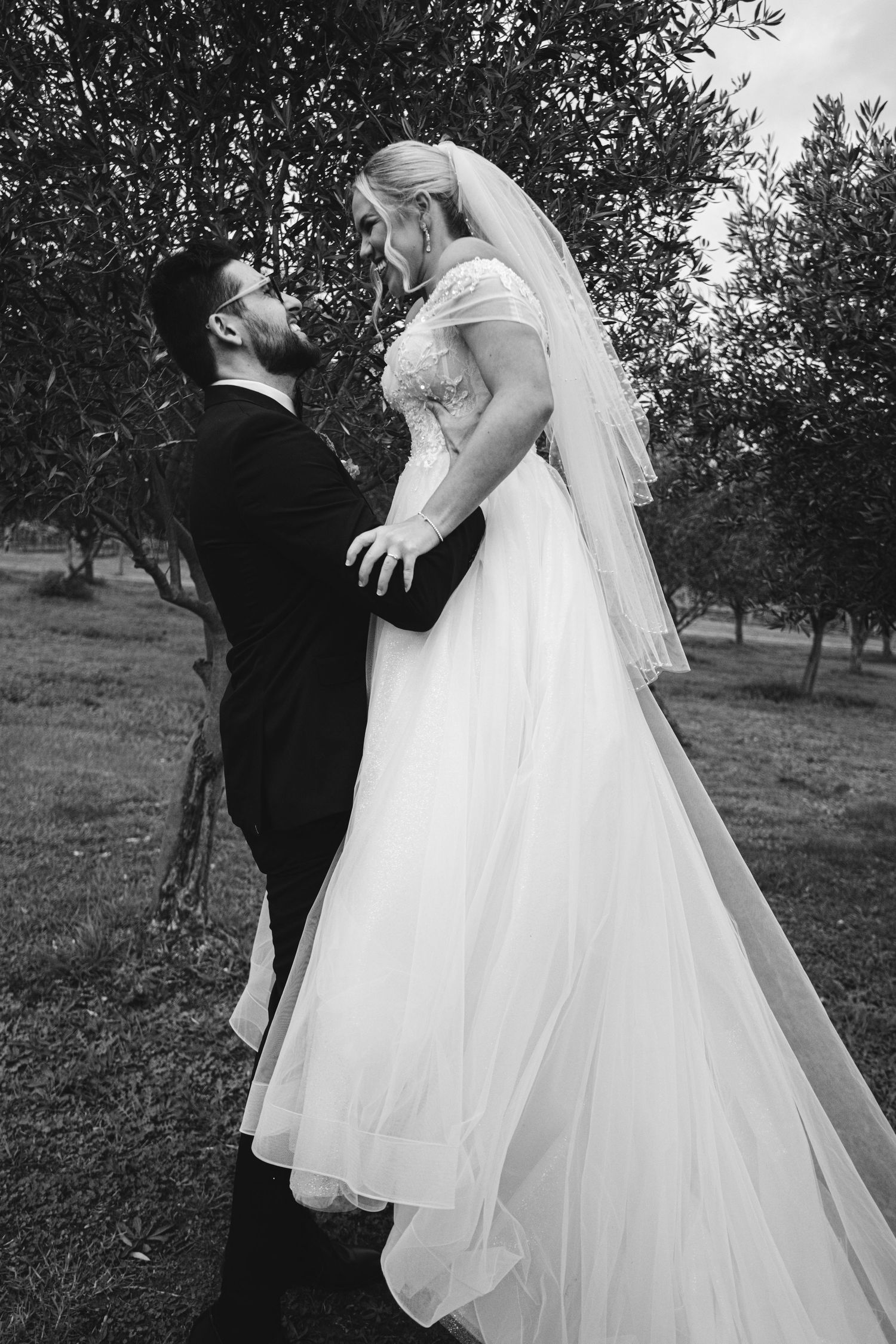 A romantic black and white wedding photo series showing a couple in an orchard with flowing white dress and veil.