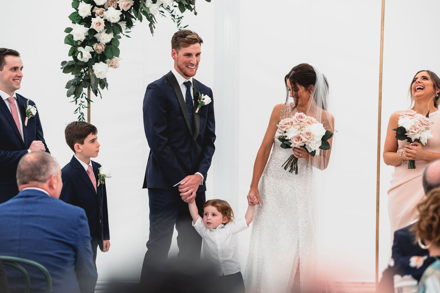 A collection of candid wedding moments showing couples and guests celebrating in an elegant white venue with floral decor.