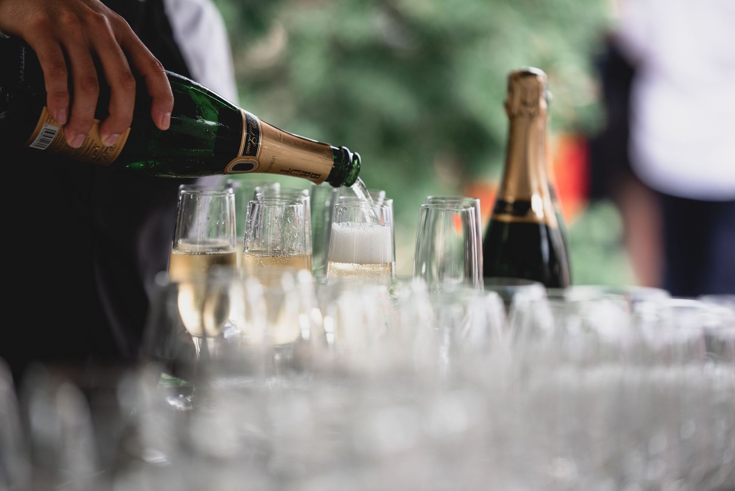 Bartender pouring drinks into multiple champagne glasses at an elegant event service.
