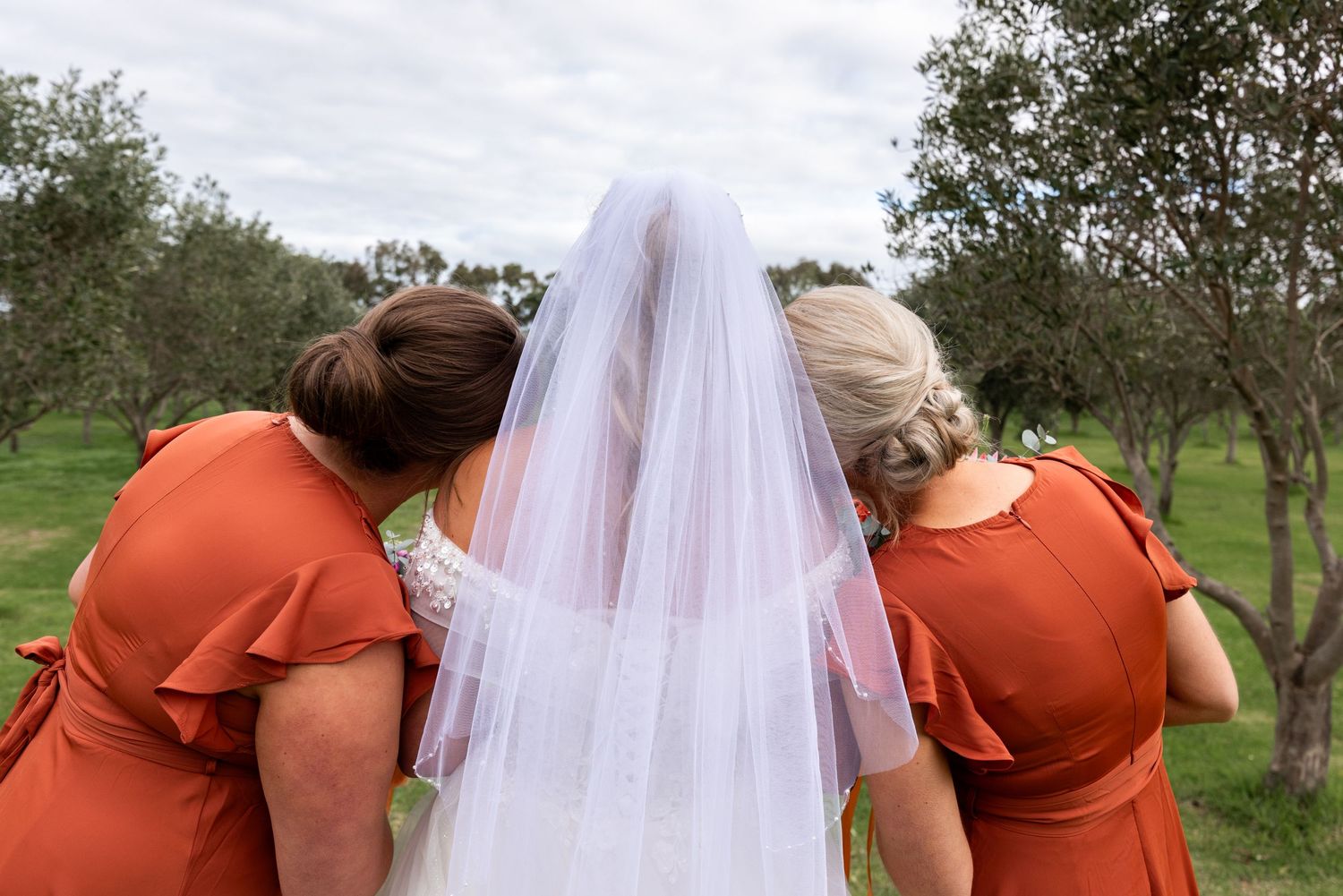 Wedding party shares a candid laughing moment outdoors with bridesmaids in orange dresses.