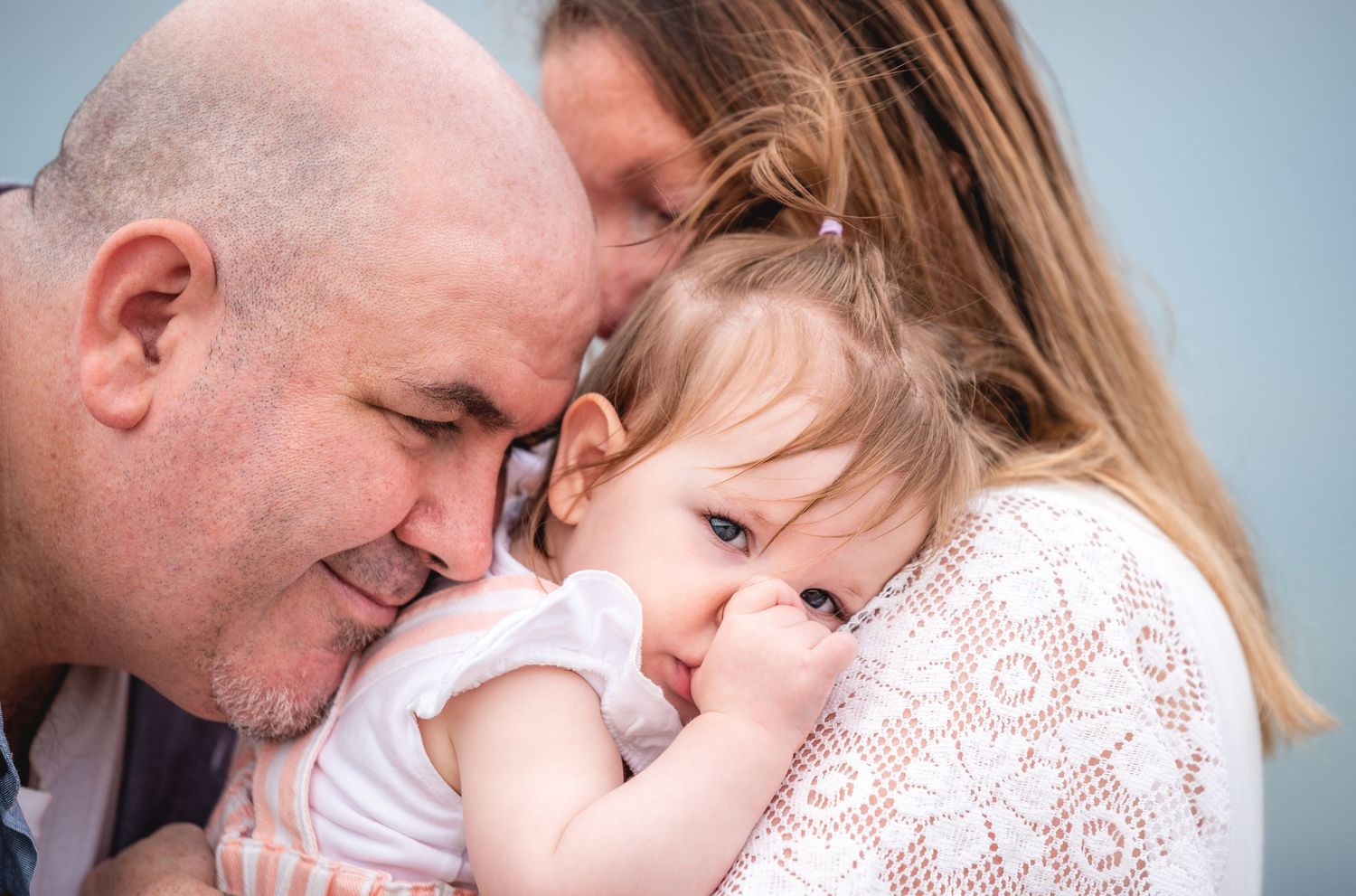 A tender family moment shows a young child being embraced in a loving hug against a soft blue background.